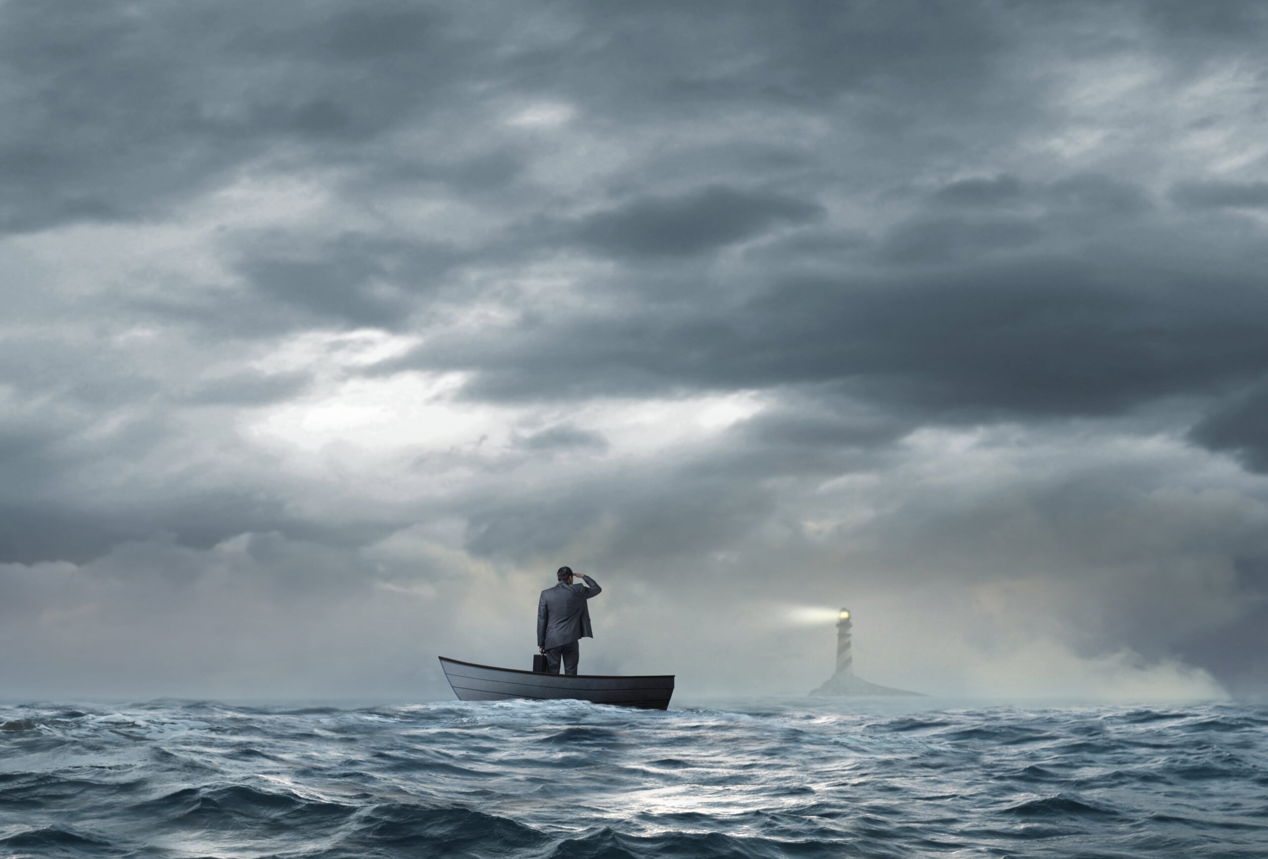 Man alone in a small boat on the open sea staring toward a lighthouse.